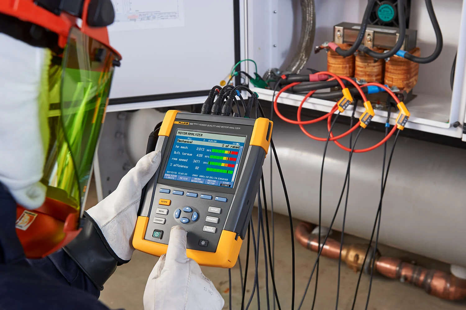A technician using a handheld power analyzer checks electrical readings on a panel, with the device displaying voltage and current data.
